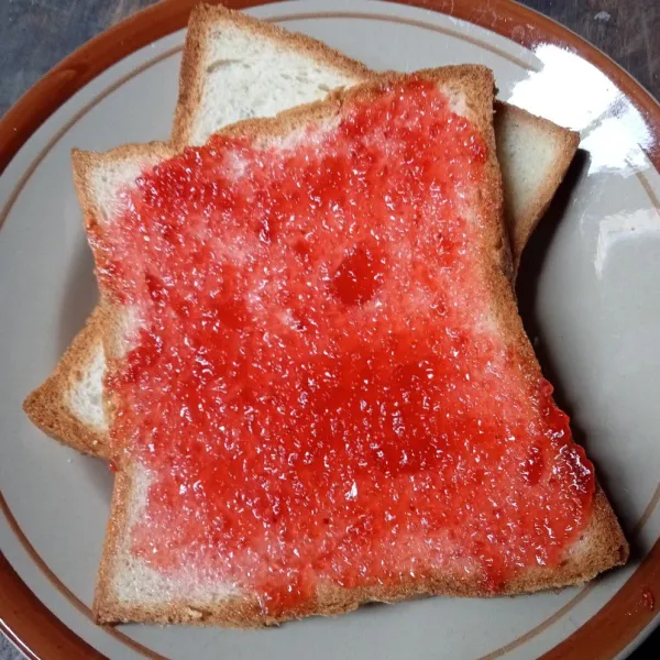 Oles permukaan roti dengan selai strawberry.
