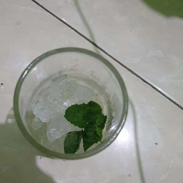 Dalam gelas air jeruk lemon. Tambahkan es batu dan daun mint.
