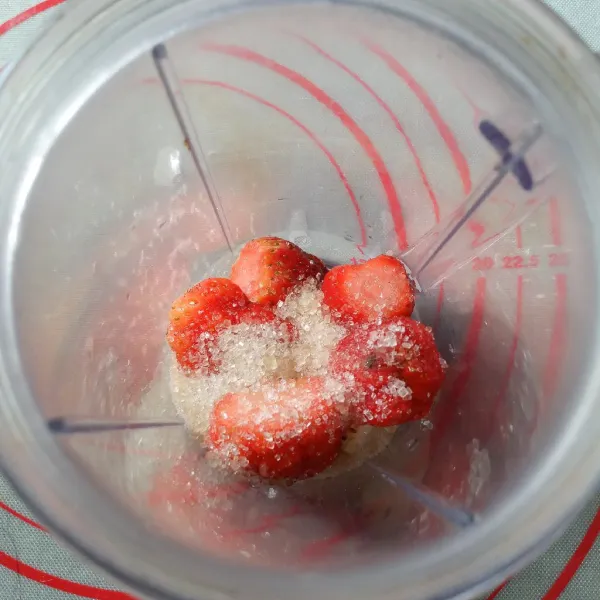 Dalam gelas blender masukkan 8 buah strawberry, yoghurt drink dan gula pasir. Blend sampai halus.