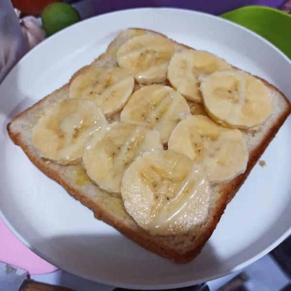 Beri irisan pisang di atas roti, lalu beri sisa kental manis putih tadi.