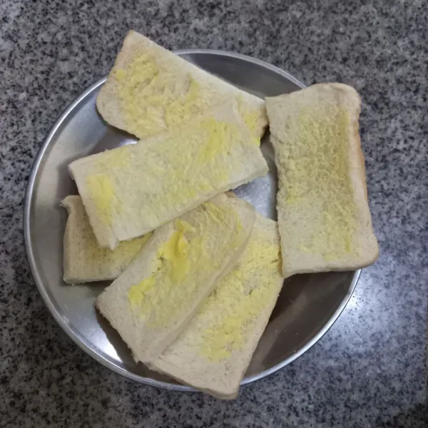 Potong roti tawar menjadi 2 bagian, kemudian olesi salah satu permukaan roti dengan margarin.