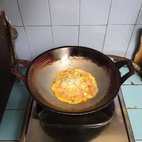 Tambahkan keju parut di atas telur. Masak hingga matang kedua sisinya.