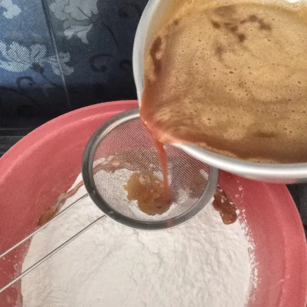 Lalu tuang larutan gula ke dalam wadah berisi tepung ketan sambil disaring.