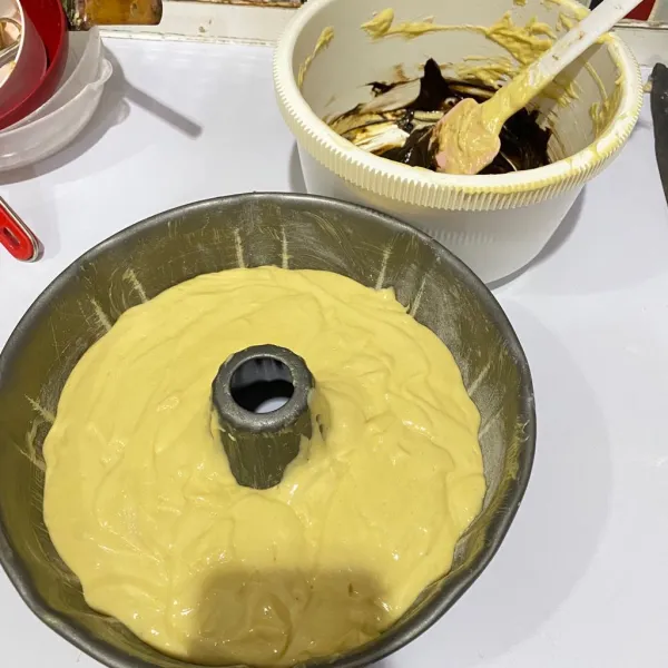 Tuang ke dalam loyang tulban yang telah diolesi margarin dan sedikit terigu. Sisakan sedikit adonan lalu beri pasta coklat, lalu aduk rata.