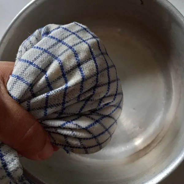 Ambil kain bersih, gunakan kain untuk memeras tahu agar airnya keluar.