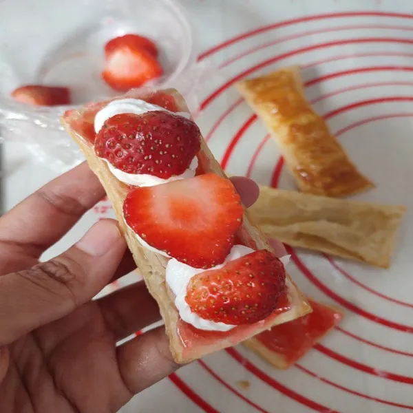 Terakhir, beri whipped cream dan potongan buah strawberry. Lalu tutup kembali dengan pastry dan taburkan gula halus di atasnya.