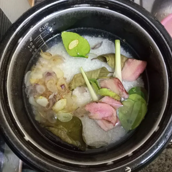 Tuang bawang yang telah ditumis pada panci rice cooker, tambahkan air secukupnya, garam, kaldu jamur, lengkuas, daun salam, daun jeruk dan serai.