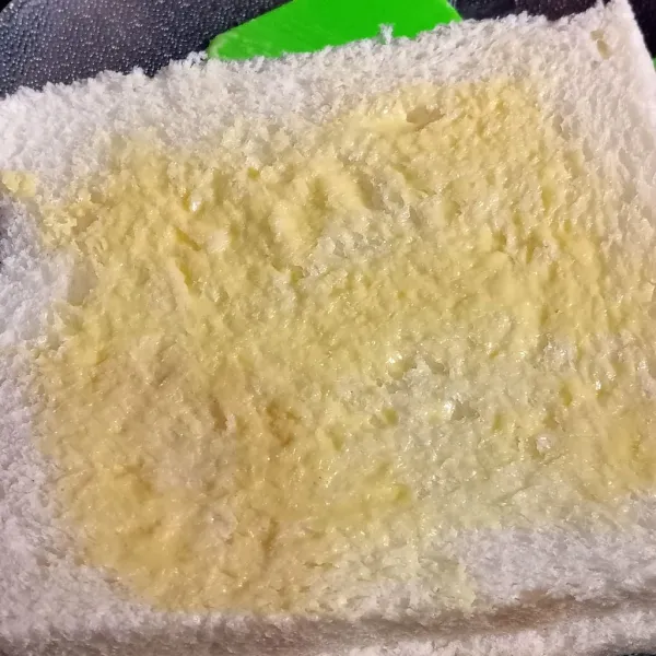 Olesi kedua sisi roti tawar dengan margarin.