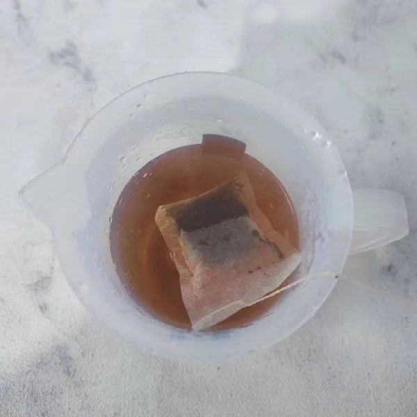 Seduh teh celup dengan air panas hingga keluar warna merahnya.