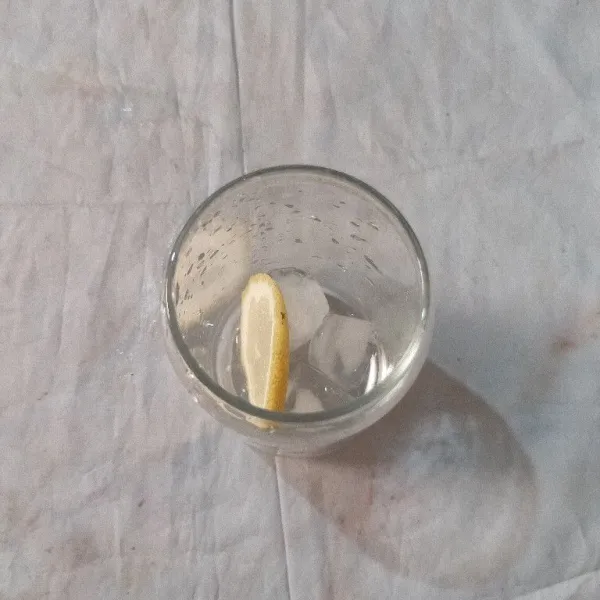 Masukkan es batu dan irisan lemon ke dalam gelas saji.