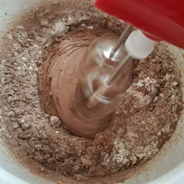 Kemudian masukkan tepung terigu, cokelat bubuk, garam, dan soda kue secara bertahap bergantian dengan susu cair sambil terus diaduk.