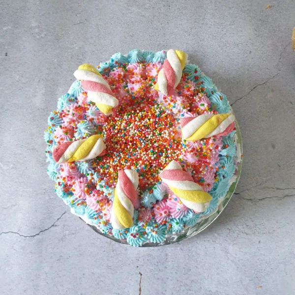 Beri hiasan atasnya dengan whippy cream yang diberi pewarna makanan  lalu taburi spinkle dan beri marsmallow. Simpan di freezer sampai setengah beku, potong dan siap disajikan🥰