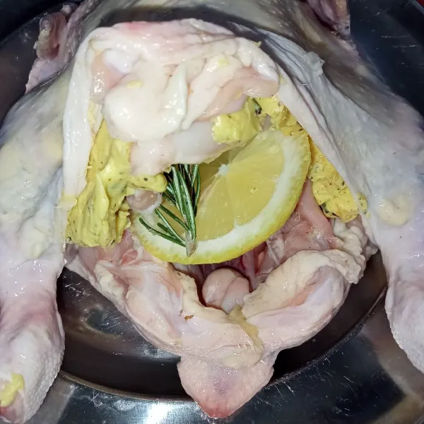 Masukkan lemon, rosemary dan bawang putih ke bagian dalam perut ayam.