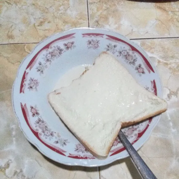 Masukkan 1 lembar roti ke dalam tepung cair. Basahi hingga 2 sisinya rata. Lakukan juga untuk 1 lembar roti lainnya.