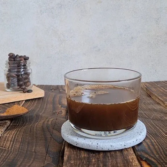 Masukkan bubuk kopi, sirup vanilla, madu, dan air hangat ke dalam gelas.