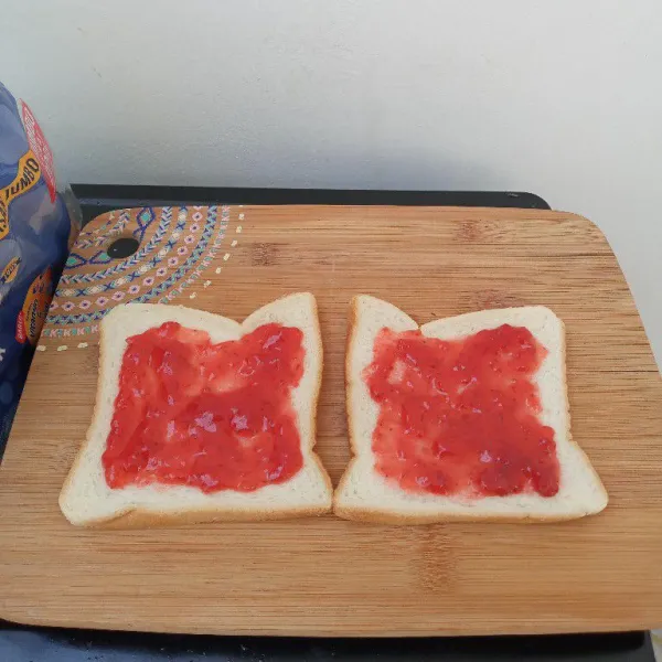 Ambil 2 lembar roti tawar, masing-masing oles dengan selai strawberry.