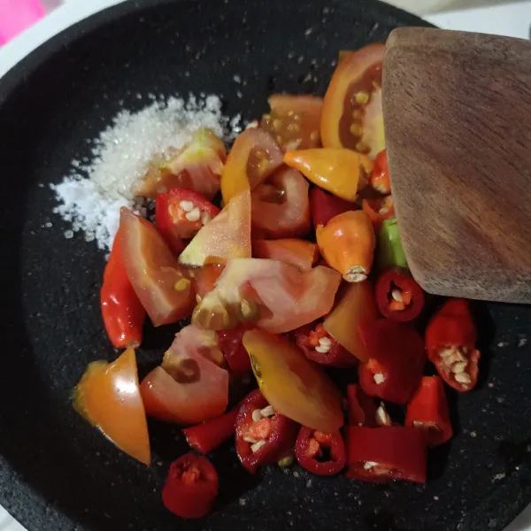 Potong-potong cabe dan tomat, letakkan dalam cobek, beri gula, garam, kaldu bubuk.