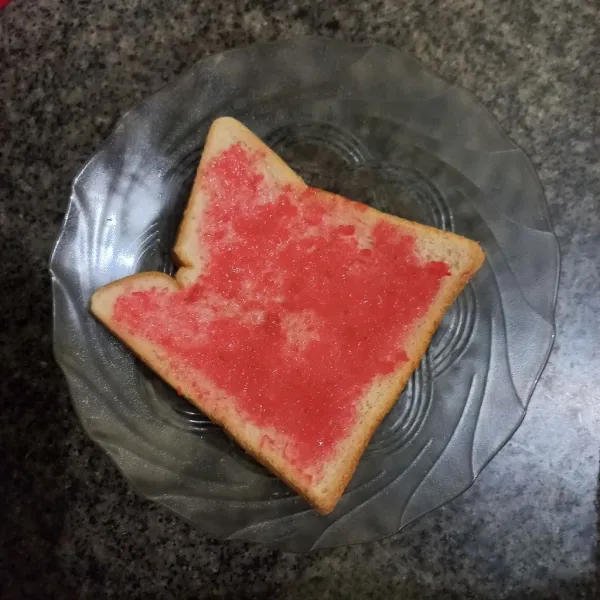 Olesi salah satu roti dengan selai strawberry.