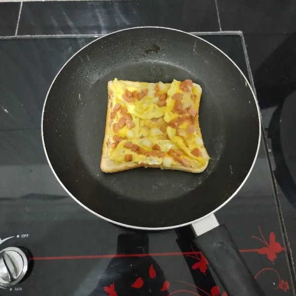 Lalu balik roti dan telur dadarnya. Rapikan pinggiran telur dadar ke tengah roti tawar. Panggang hingga matang. Angkat.