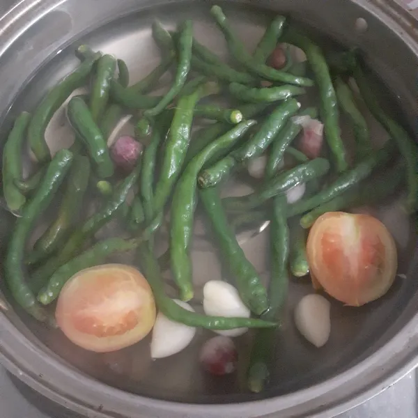 Didihkan air dan rebus cabe hijau, tomat, bawang merah, bawang putih hingga empuk. Angkat dan tiriskan.