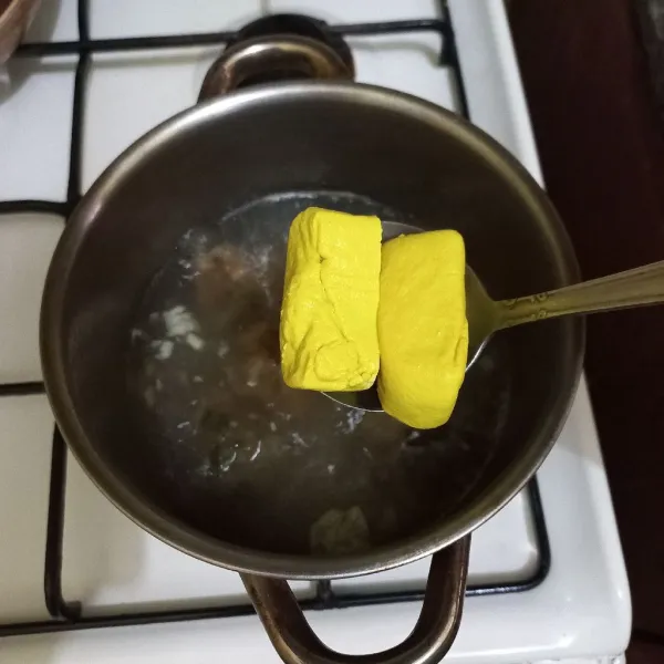 Masukkan potongan tahu kuning ke dalam panci rebusan.
