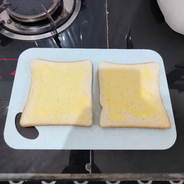 Oles satu sisi roti tawar dengan margarin.