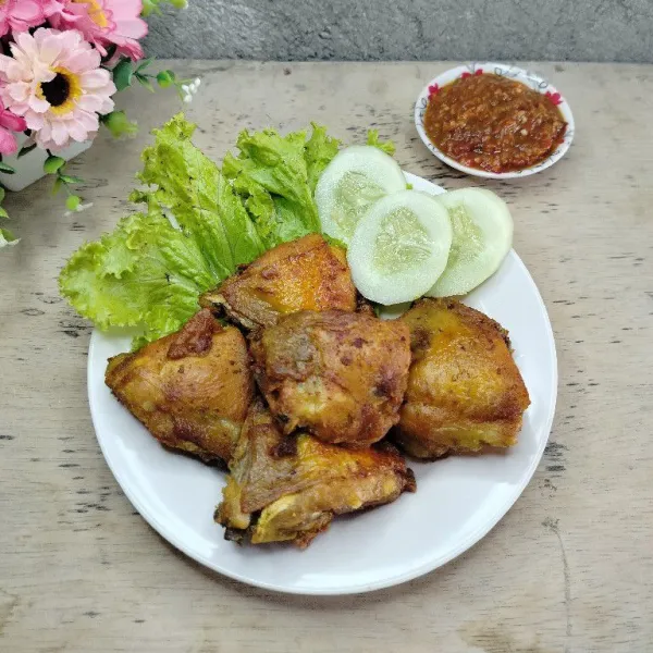 Tata ayam goreng di piring. Sajikan dengan sambal terasi dan lalapan timun serta daun selada.