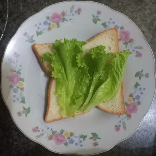 Tata daun selada di atas roti.