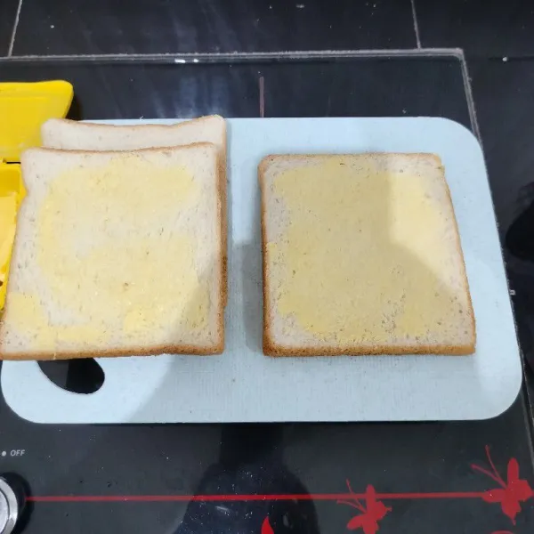 Oles 2 buah roti tawar dengan margarin tipis-tipis.