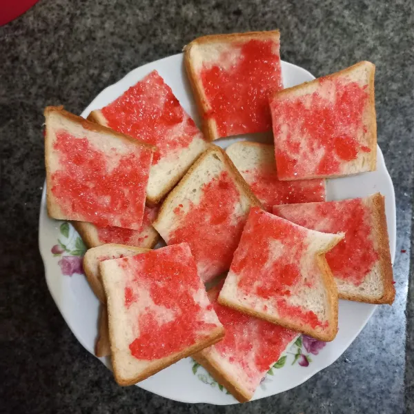Olesi roti tawar dengan selai strawberry, ratakan dan potong-potong roti.