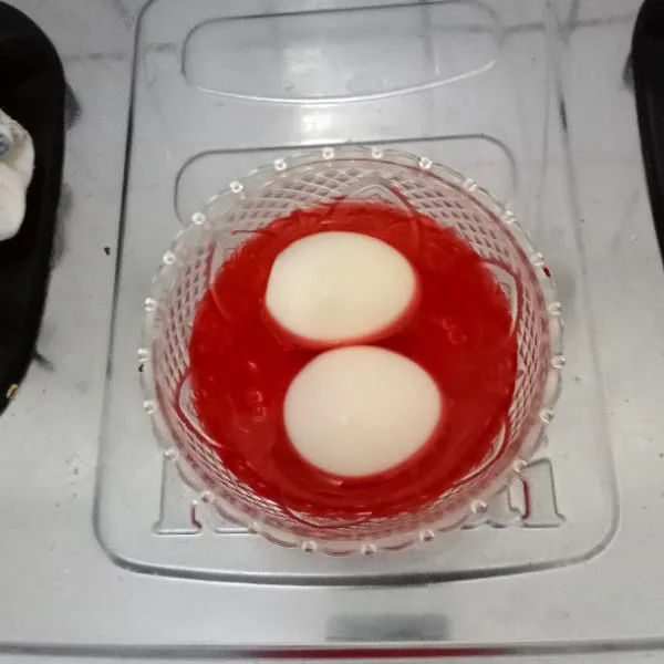 Masukkan air dalam wadah. Masukkan pewarna merah. Aduk rata. Masukkan telur rebus kedalamnya. Diamkan sebentar & sisihkan