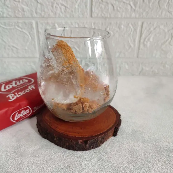 Masukkan es batu ke dalam gelas, lalu tambahkan biskuit lotus biscoff.