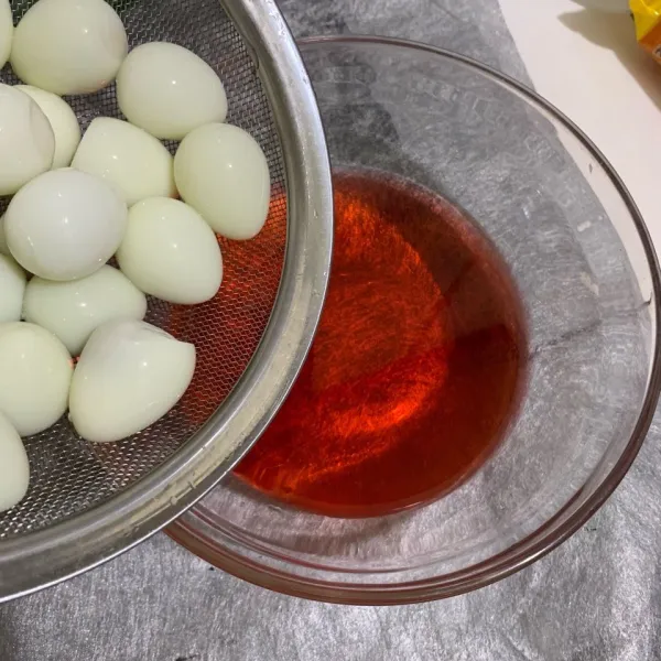 Siapkan air dan berikan pewarna merah. Aduk rata. Masukkan telur puyuh rebus ke dalam larutan air merah hingga telur berubah warna.