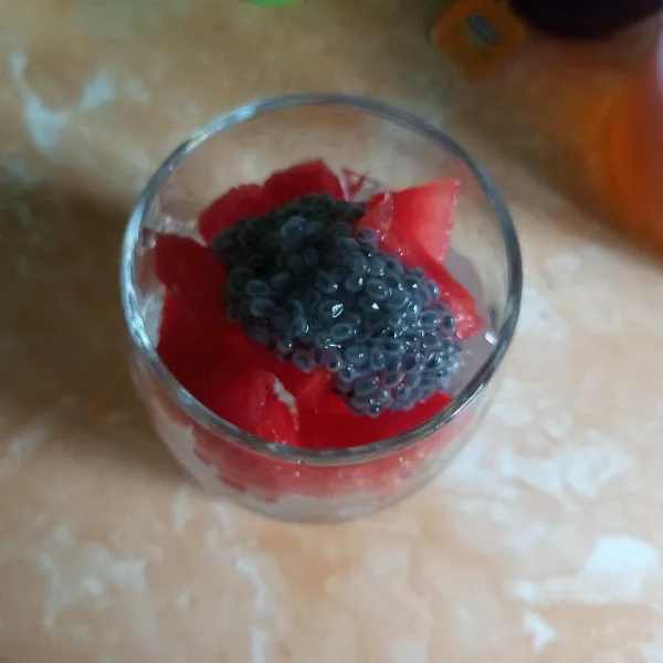 Siapkan gelas tambahan es batu secukupnya kemudian tambahkan semangka dan biji selasih.