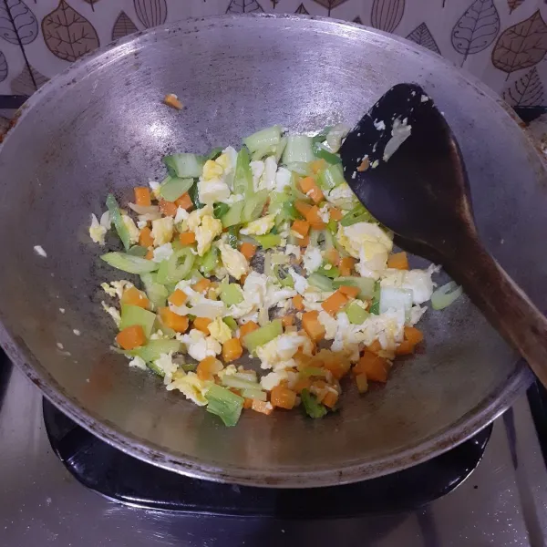 Tambahkan sayuran yang keras, yaitu wortel dan batang bok choy. Tumis hingga layu.