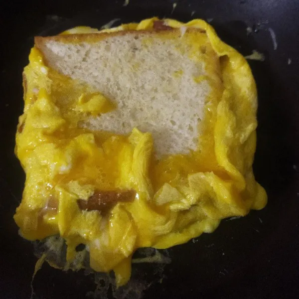 Selanjutnya tuangkan telur yang sudah dikocok dengan garam dan lada. Beri roti tawar diatasnya, lalu rapikan pinggirannya.