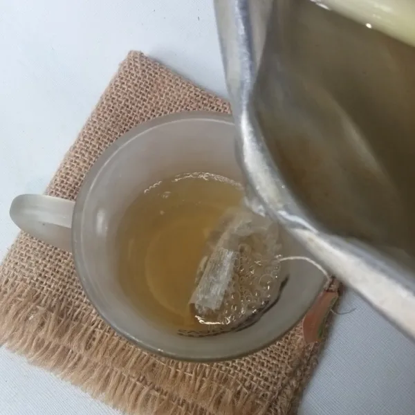 Siapkan gelas dan teh celup, lalu tuang air rebusan serai.