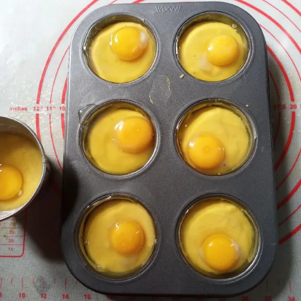 Tuang adonan dalam cetakan muffin yang sudah dioles tipis dengan minyak/ papercup setinggi setengah cetakan. Pecahkan telur masing-masing satu butir di atas adonan kue. Taburi secubit garam.