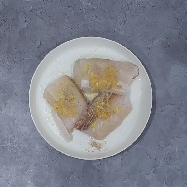 Haluskan bawang putih. Campur ikan dengan bawang putih halus, kaldu bubuk dan lada bubuk. Aduk rata. Marinasi selama minimal 30 menit agar meresap.