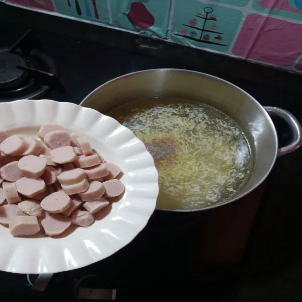 Pindahkan dalam panci, beri air, masukkan garam, penyedap rasa, merica bubuk dan irisan sosis.