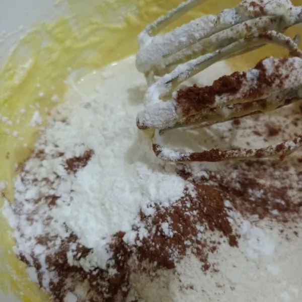 Tambahkan tepung terigu, cokelat bubuk yang telah dicampur baking powder, bergantian dengan susu cair. Sambil dimixer kecepatan rendah. Lakukan sampai habis.