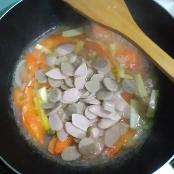 Tambahkan wortel dan putren, tumis sebentar, tambahkan air, masak hingga sayuran setengah matang, tambahkan irisan bakso dan sosis, aduk rata