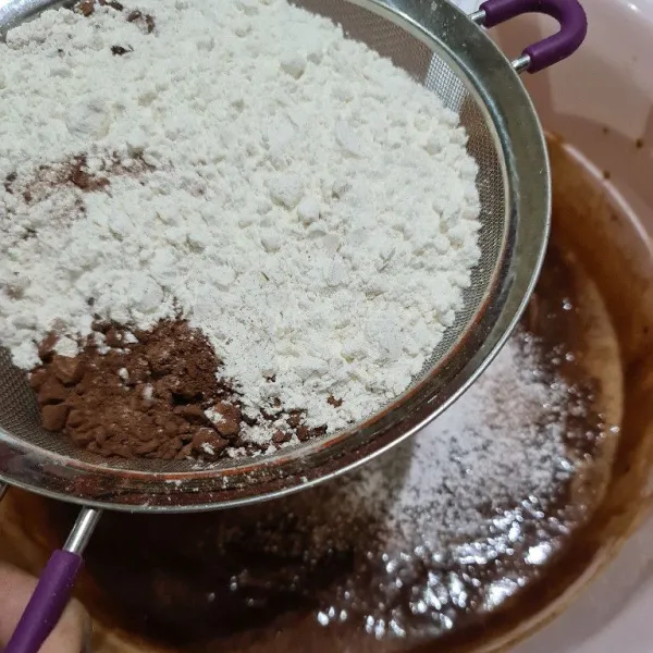 Ayak tepung terigu dan coklat bubuk ke atas adonan coklat.