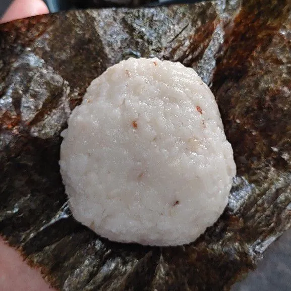 Ambil 1 lembar nori, bagi menjadi 2 bagian lalu bungkus nasi dengan nori sampai semua permukaan nasi tertutup.