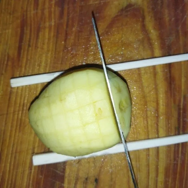 Kupas kentang lalu cuci bersih. Siapkan sumpit, taruh di sisi kentang, potong secara vertikal dan horizontal hingga membentuk kotak-kotak.