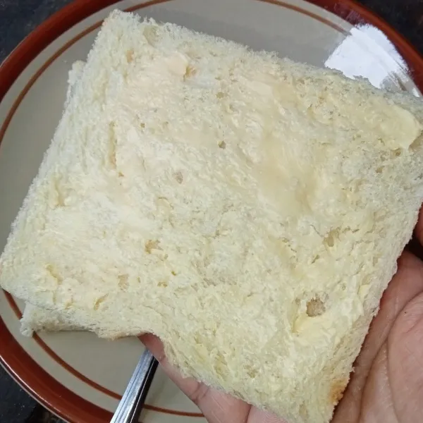 Oles tipis satu sisi roti dengan margarin.