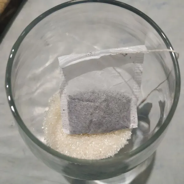 Masukkan gula pasir dan teh celup ke dalam gelas.