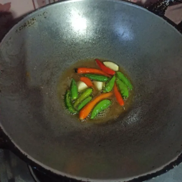 Goreng cabai rawit dan bawang putih hingga layu.