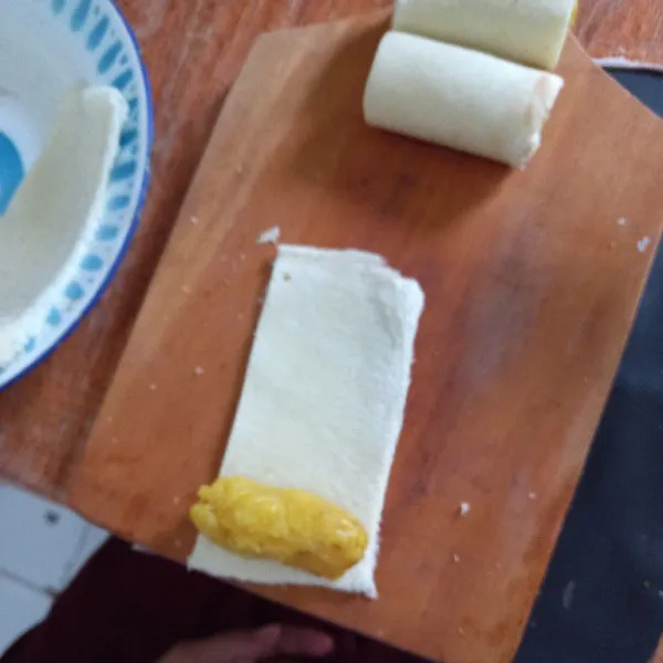 Ambil roti tawar, taruh pisang di ujung permukaan roti dan gulung, beri ujungnya perekat dengan air biasa.