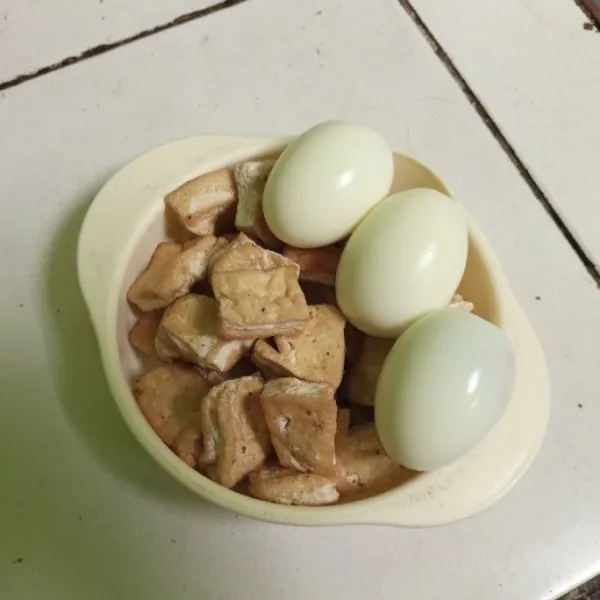 Bersihkan telur lalu rebus dan kupas. Selanjutnya, potong-potong tahu sesuai selera dan goreng hingga setengah matang.